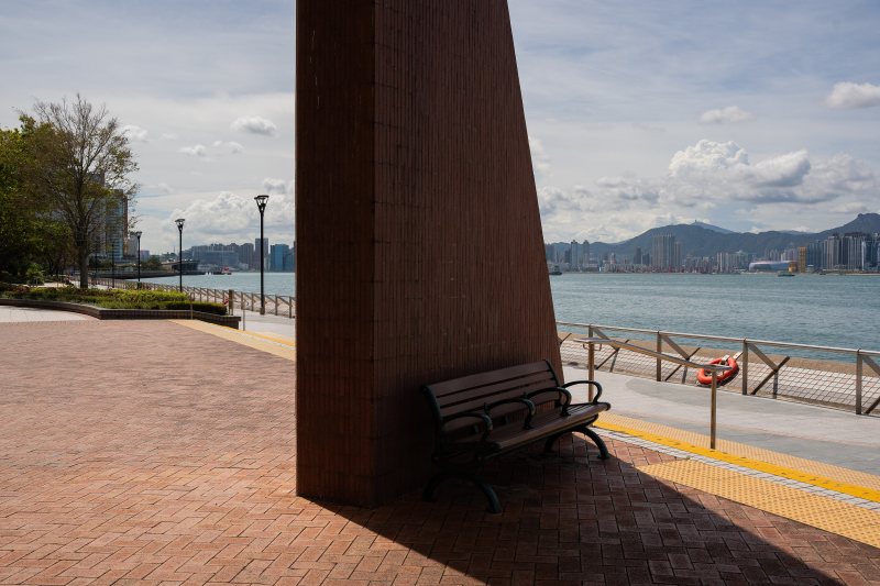 Leere Bank im Schatten an einer sonnigen Uferpromenade
