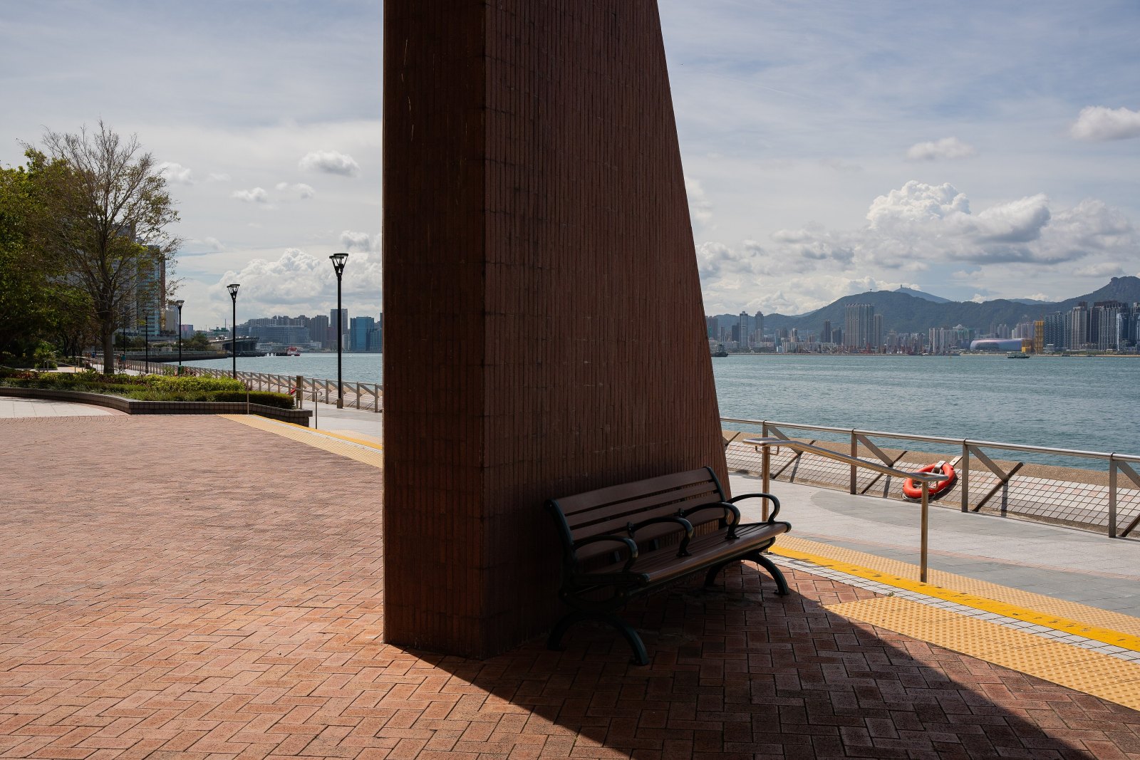 Leere Bank im Schatten an einer sonnigen Uferpromenade