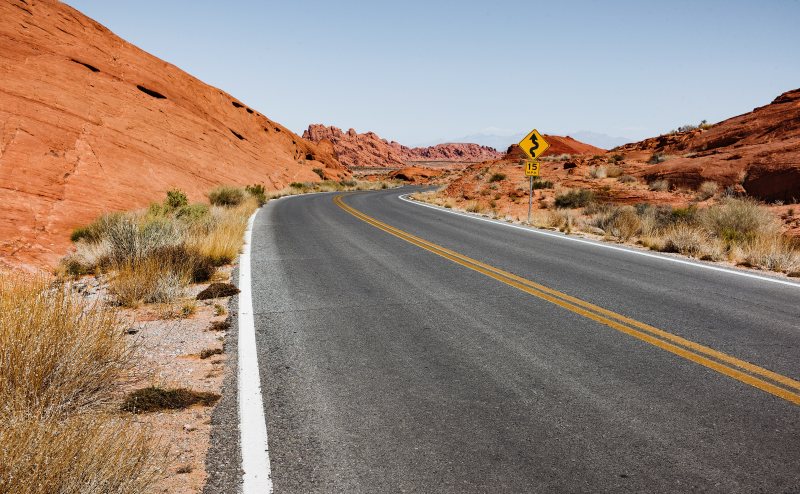 Leere Straße durch eine trockene rote Felslandschaft unter blauem Himmel