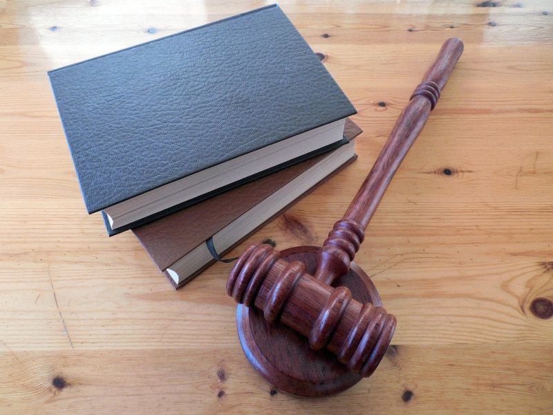 Ein hölzerner Richterhammer liegt neben drei geschlossenen Gesetzbüchern.